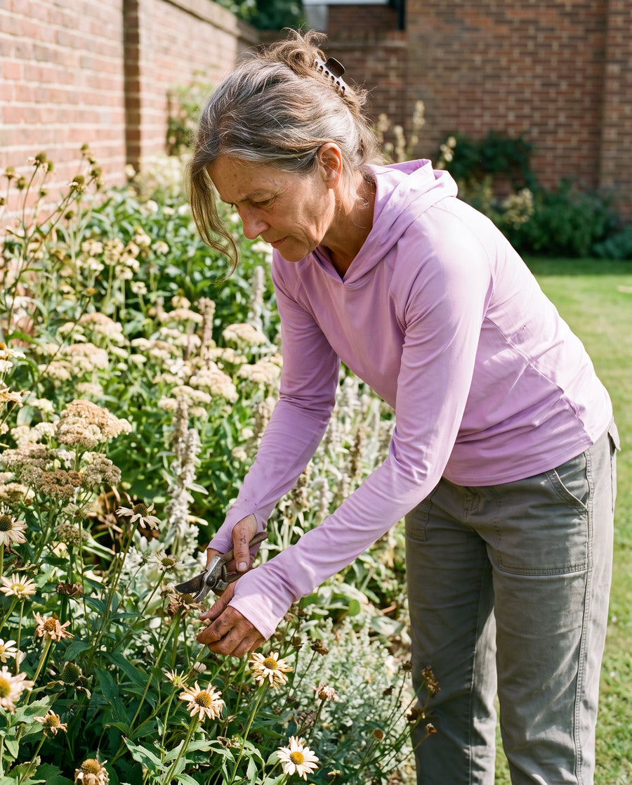 Woman deadheading a flower border in the lilac sun hoodie in the midday sun