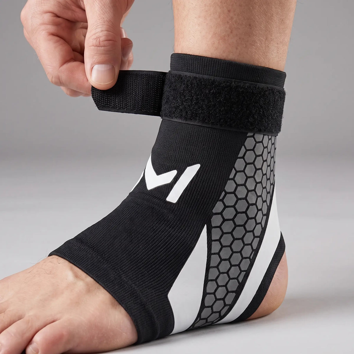 Hand wrapping the hook-and-loop strap of the ankle support brace round the ankle