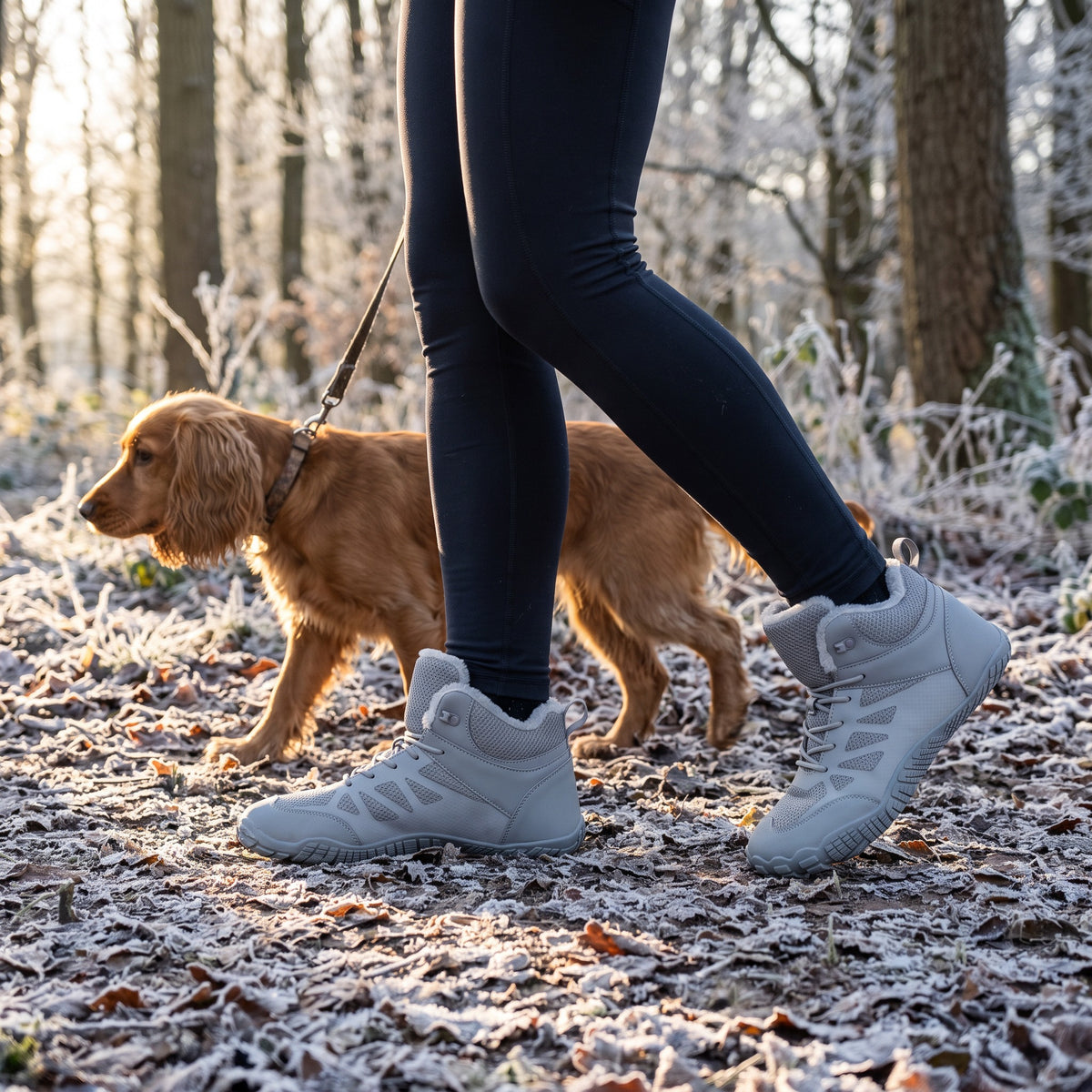 Woman walking a spaniel on a frosty woodland path in the barefoot winter boots