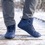 Barefoot winter boots in Navy worn on a snowy boardwalk, wide toe box from the front