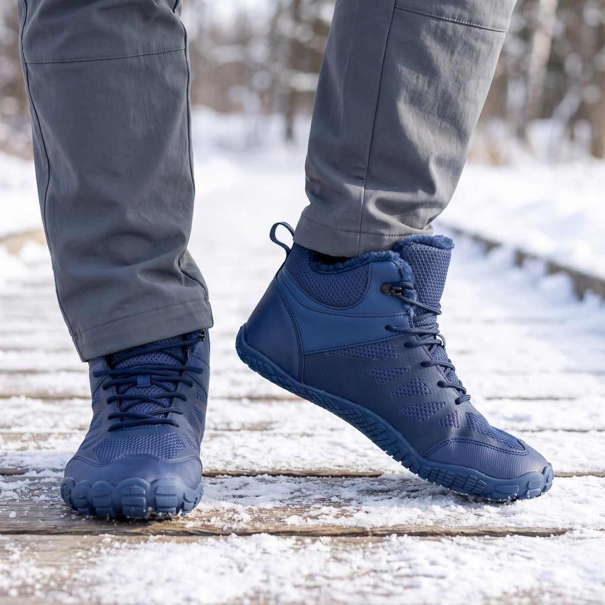 Barefoot winter boots in Navy worn on a snowy boardwalk, wide toe box from the front