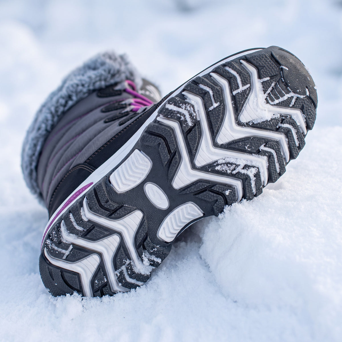 Deep chevron rubber tread of the women's snow boots with packed snow in the lugs