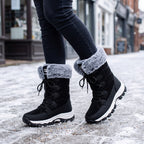Black women's winter boots with faux fur cuff worn on an icy town pavement