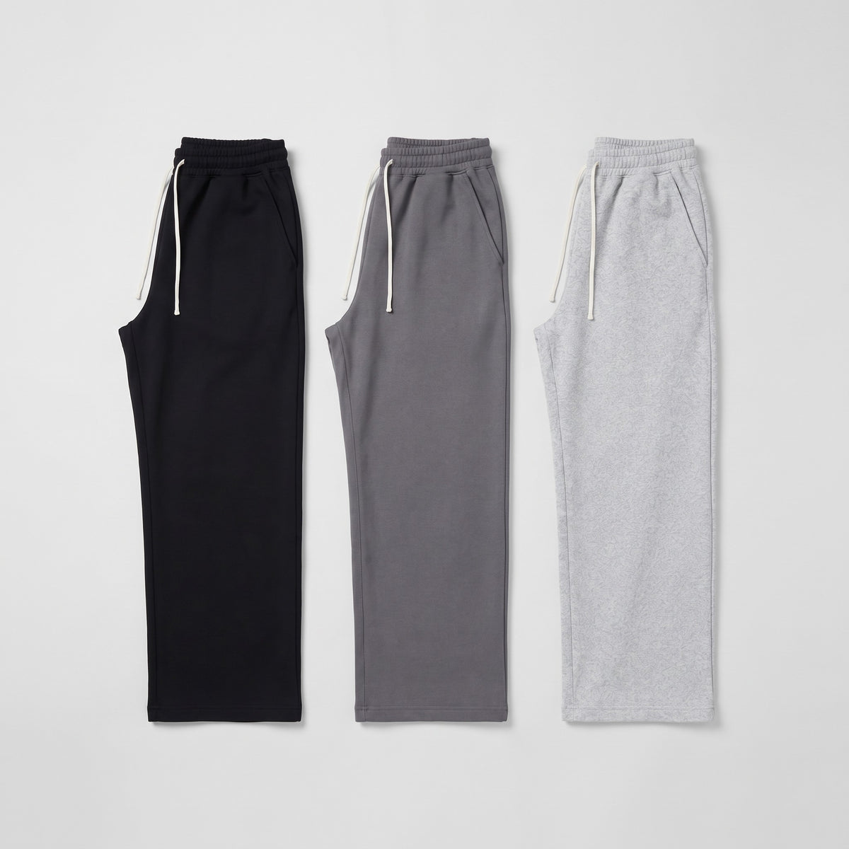 Men's wide leg joggers in Black, Grey and Light Grey laid flat side by side