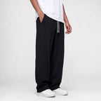 Black baggy straight leg joggers, three-quarter side view with the open hem over white trainers