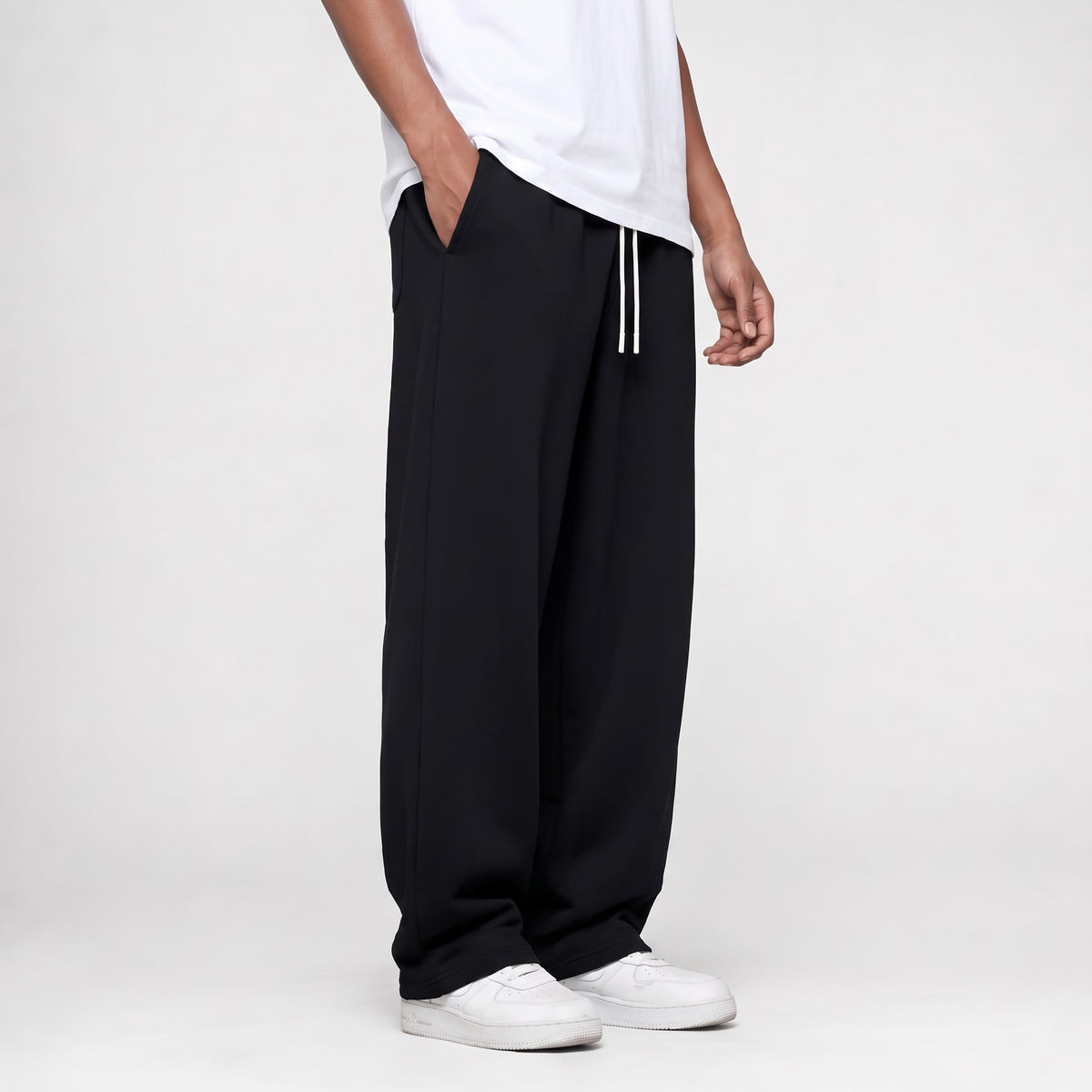 Black baggy straight leg joggers, three-quarter side view with the open hem over white trainers
