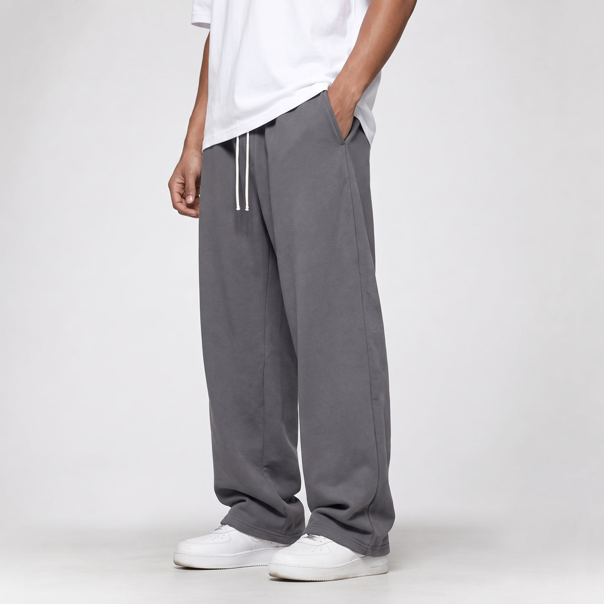 Grey baggy straight leg joggers, three-quarter side view with the open hem over white trainers