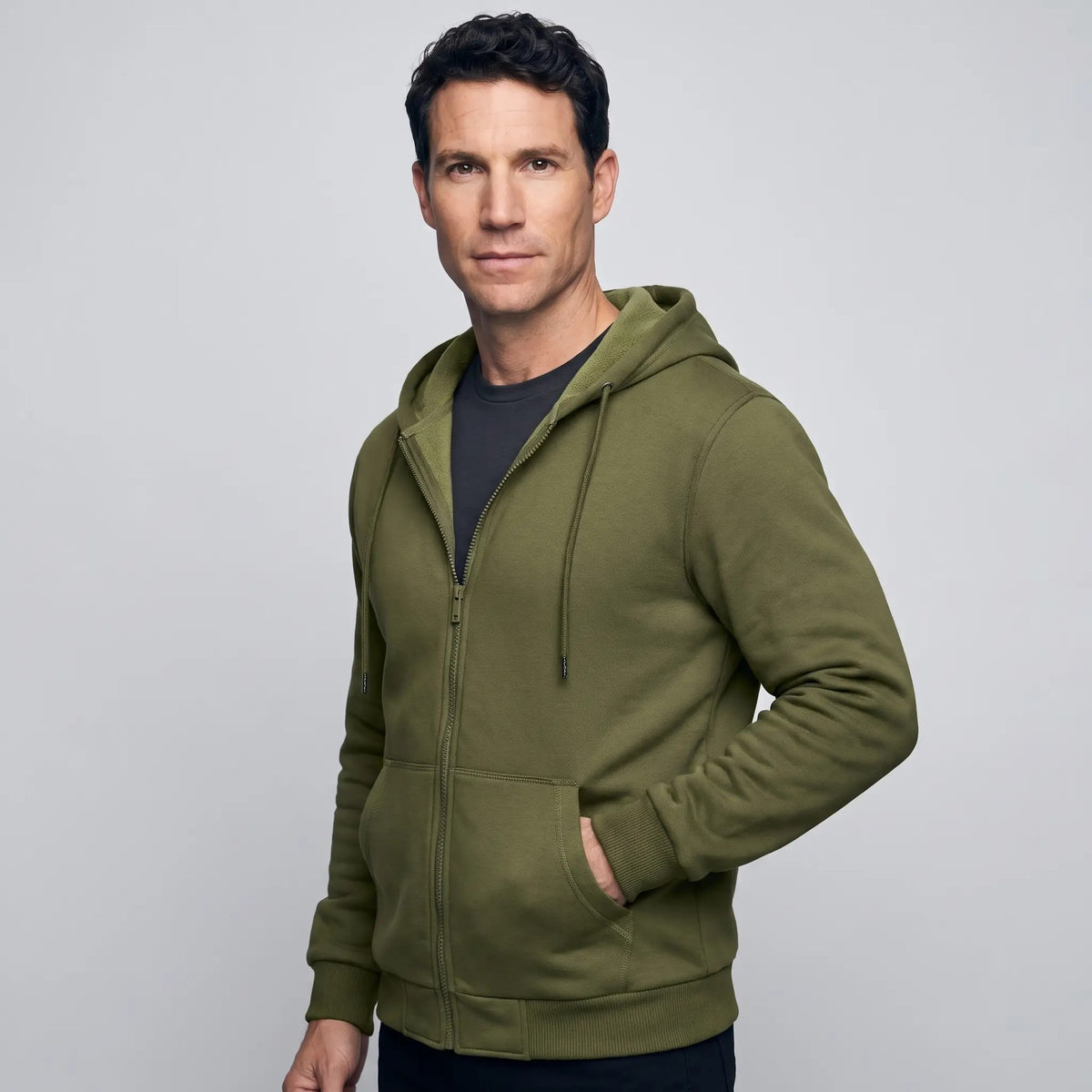 Three-quarter view of a man in the Army Green zip up hoodie, hand in the pocket