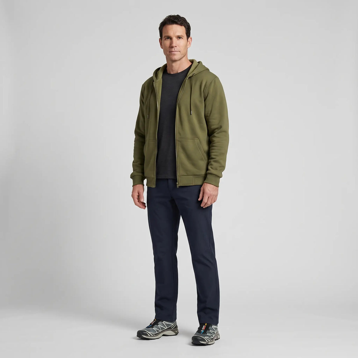 Full-length view of a man wearing the zip up hoodie with dark trousers