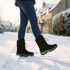 Woman walking down a snowy village lane in the Black fur lined winter boots