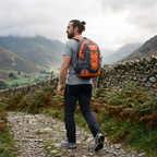 Man walking a stony Lake District fell path wearing the Terrabound 30L hiking rucksack in Orange