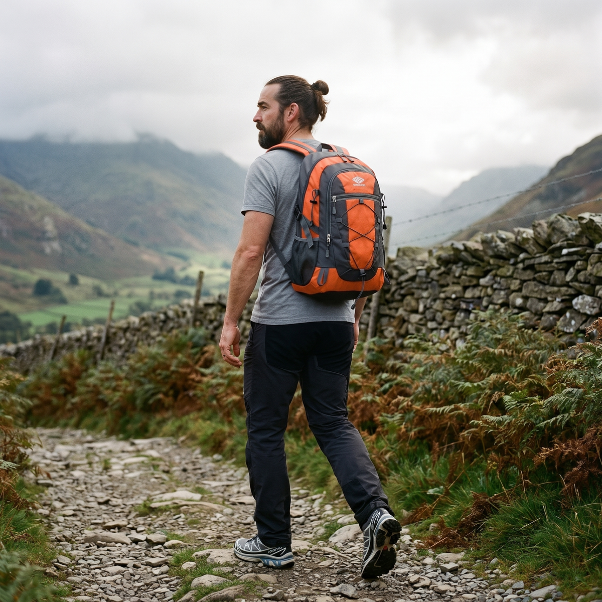 Man walking a stony Lake District fell path wearing the Terrabound 30L hiking rucksack in Orange