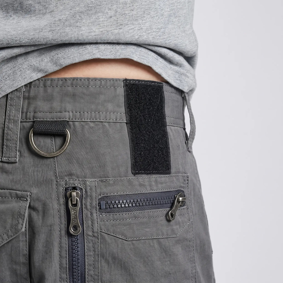 Waistband close-up with metal D-ring, hook-and-loop panel and zipped hip pocket