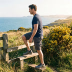 Walker in grey cargo shorts climbing a stile on a coastal path