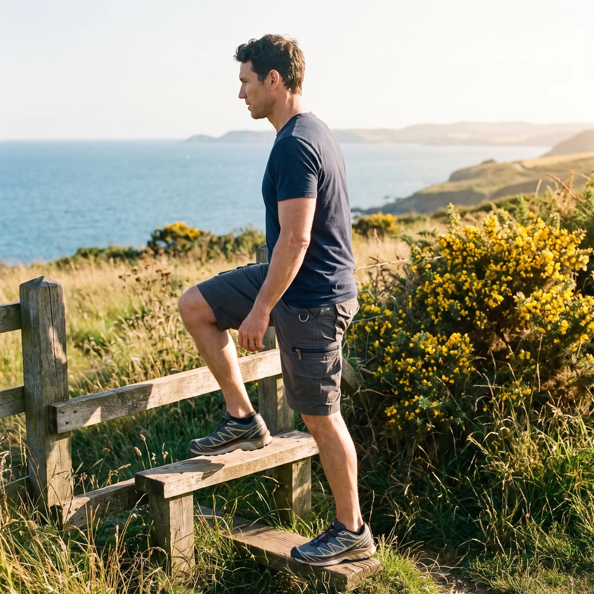 Walker in grey cargo shorts climbing a stile on a coastal path