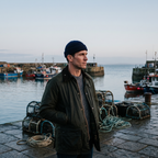 Man in a navy fisherman beanie on a harbour quay in Britain at dawn