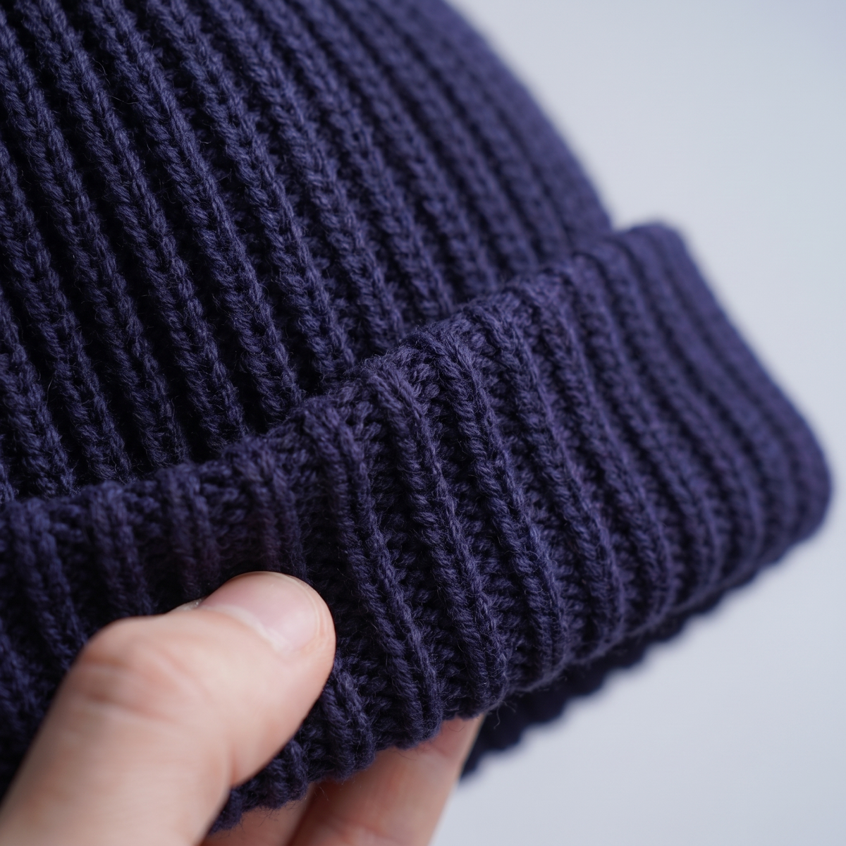 Close up of the chunky rib knit and turned cuff stretching between finger and thumb