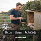 Walker taking coins from the zip card holder at a farm honesty box, cord clipped to his belt loop
